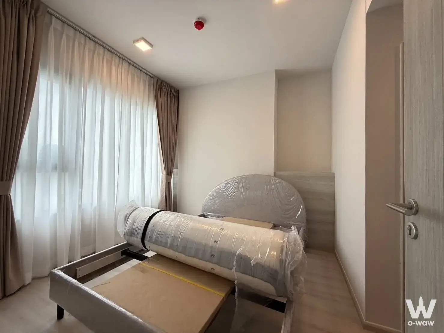 Unfurnished bedroom in COBE Ratchada-Rama 9 condo with light wood bed frame and large window