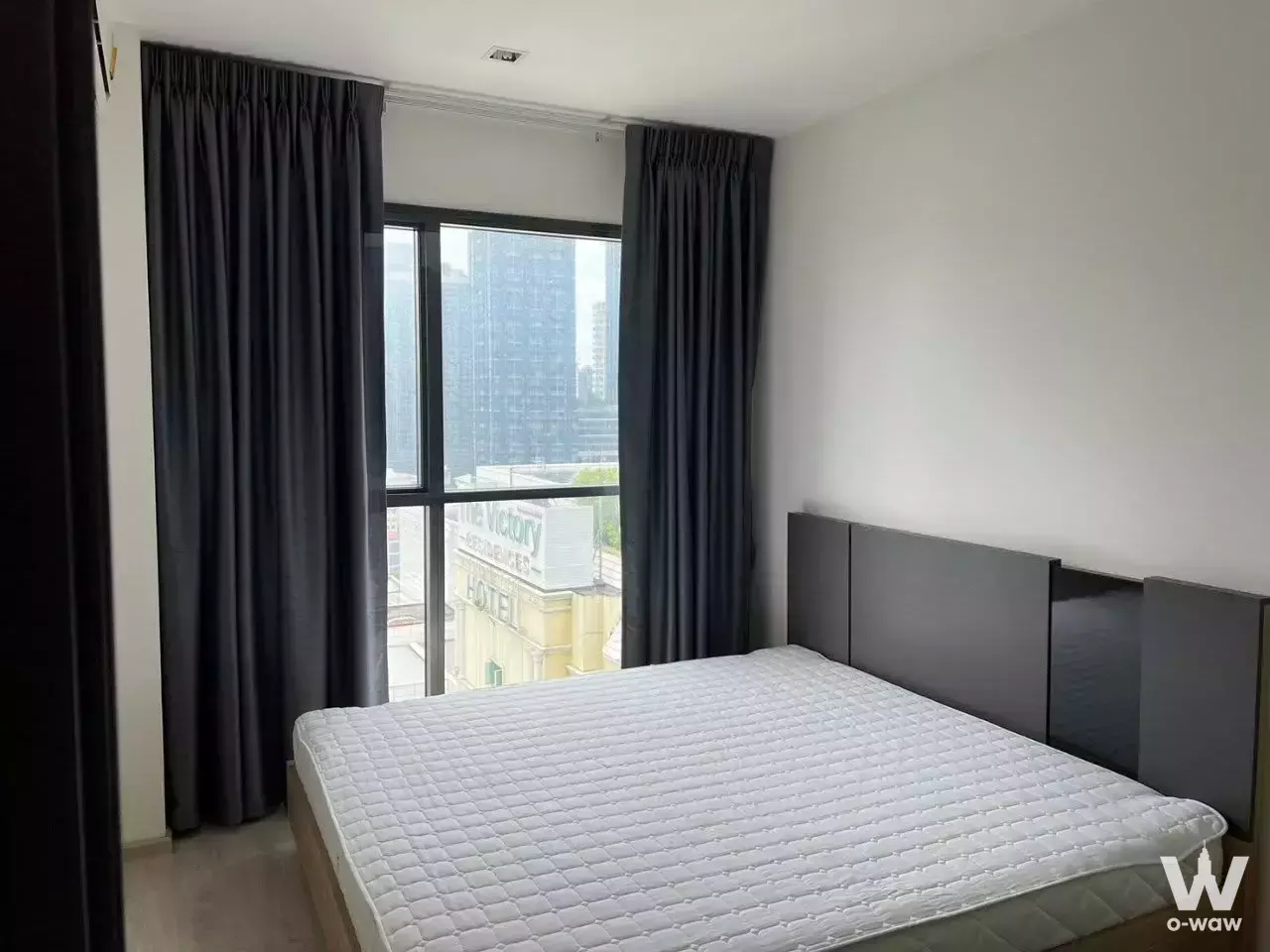 Bedroom in Rhythm Rang Nam condo with queen bed, grey headboard, and large window overlooking city