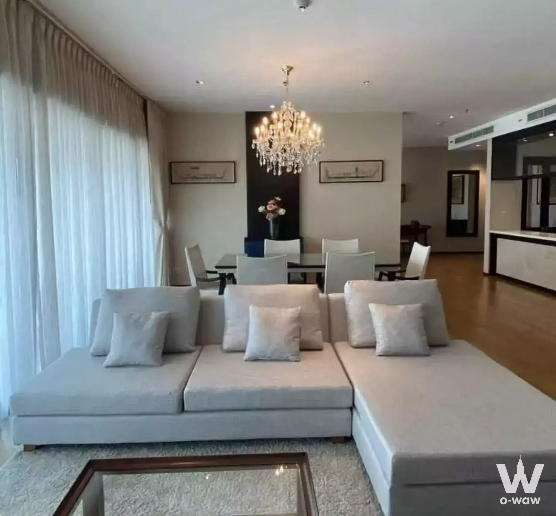 Spacious open-plan living room in The Madison 3-bed condo featuring L-shaped grey sofa, hardwood floors, and crystal