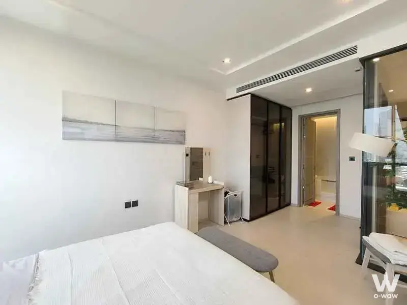 Master bedroom in The Room Sukhumvit 38 condo with queen bed, dark smoked glass wardrobe, and minimalist neutral decor
