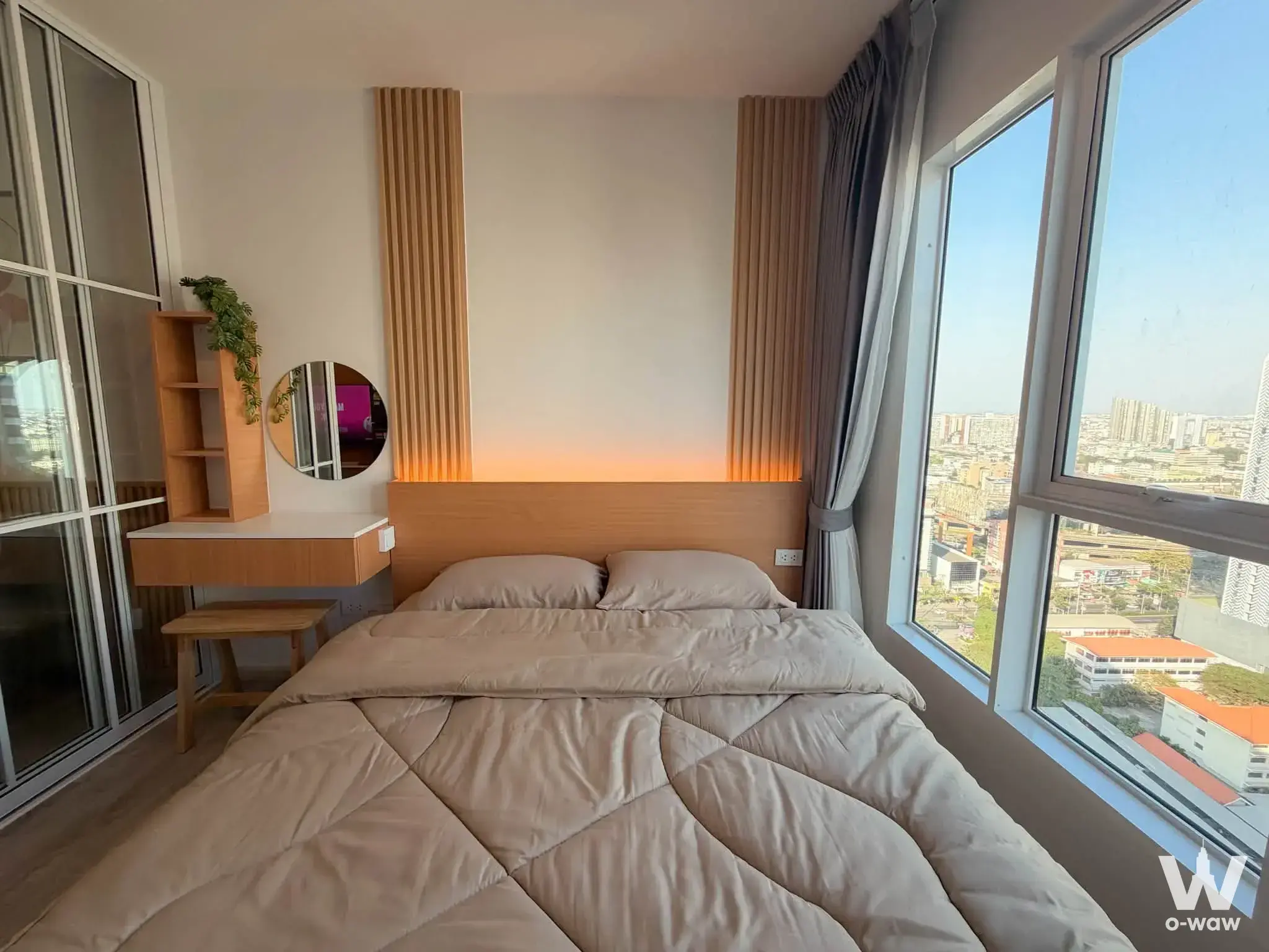 Bright bedroom in Regent Home Bangna with a queen bed, wood slat headboard, floating desk, and floor-to-ceiling window with