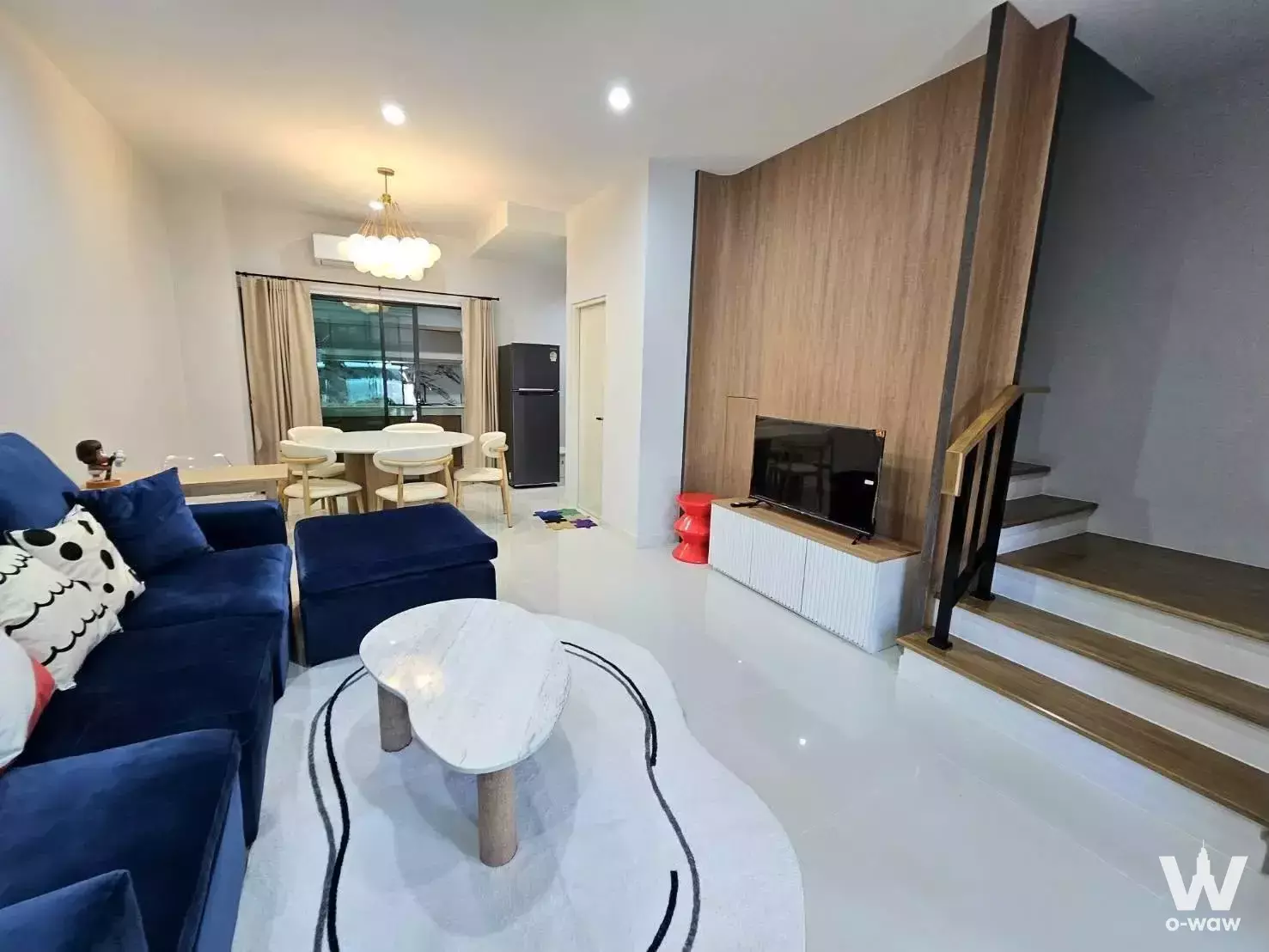 Open-plan living area in 3-bed Baan Klang Muang townhouse with navy sofa, marble coffee table, and wooden staircase