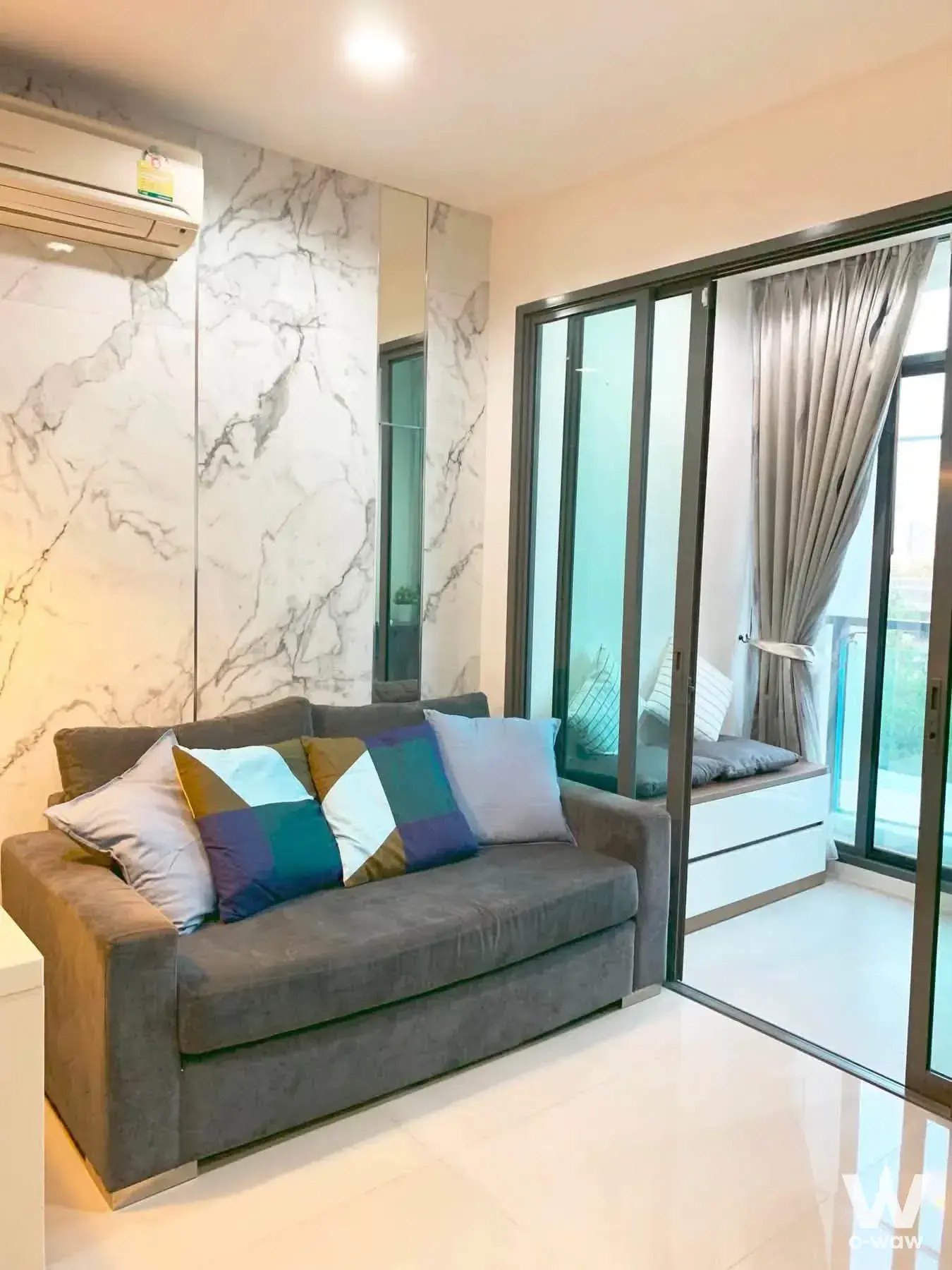 Ideo Blucove Sathorn 2-bed condo living room with grey sofa, marble feature wall, and built-in window seat