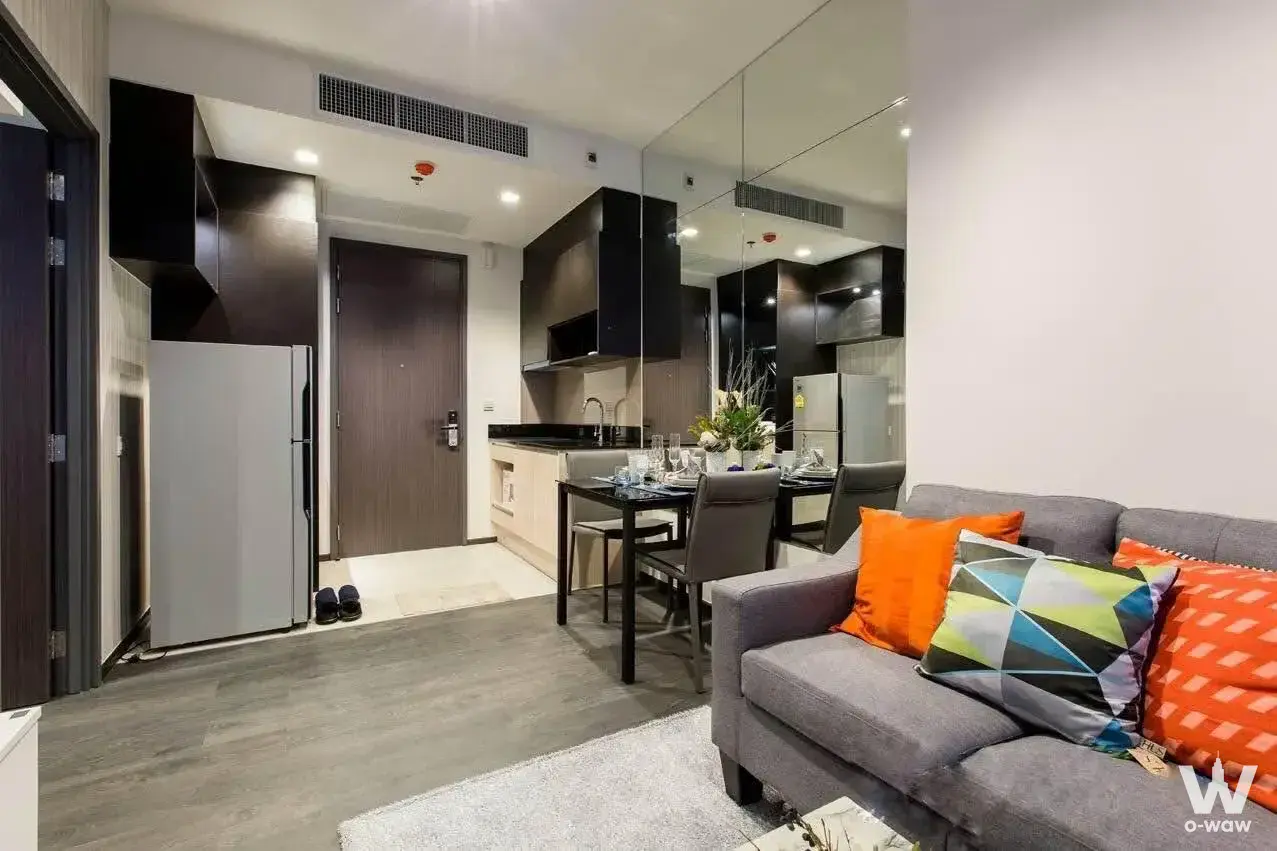 Open-plan living and dining area in a 1-bed condo at The Edge Sukhumvit 23 featuring grey sofas and black glass table
