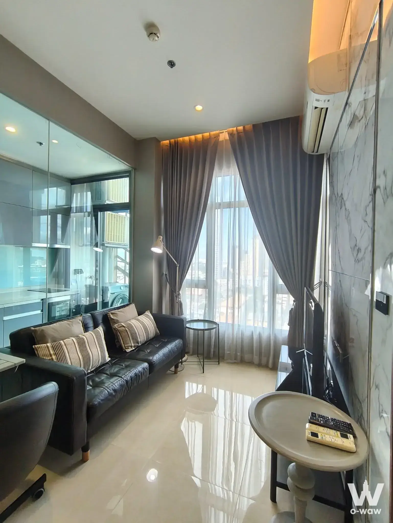 Modern 1-bed condo living room in Mayfair Place Sukhumvit 50 with leather sofa and city skyline view