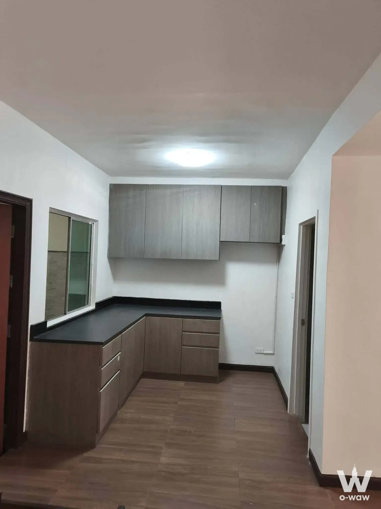 Unfurnished kitchen in Pruksa Ville 66/1 townhouse with wood-look cabinets, black countertop, and glass window