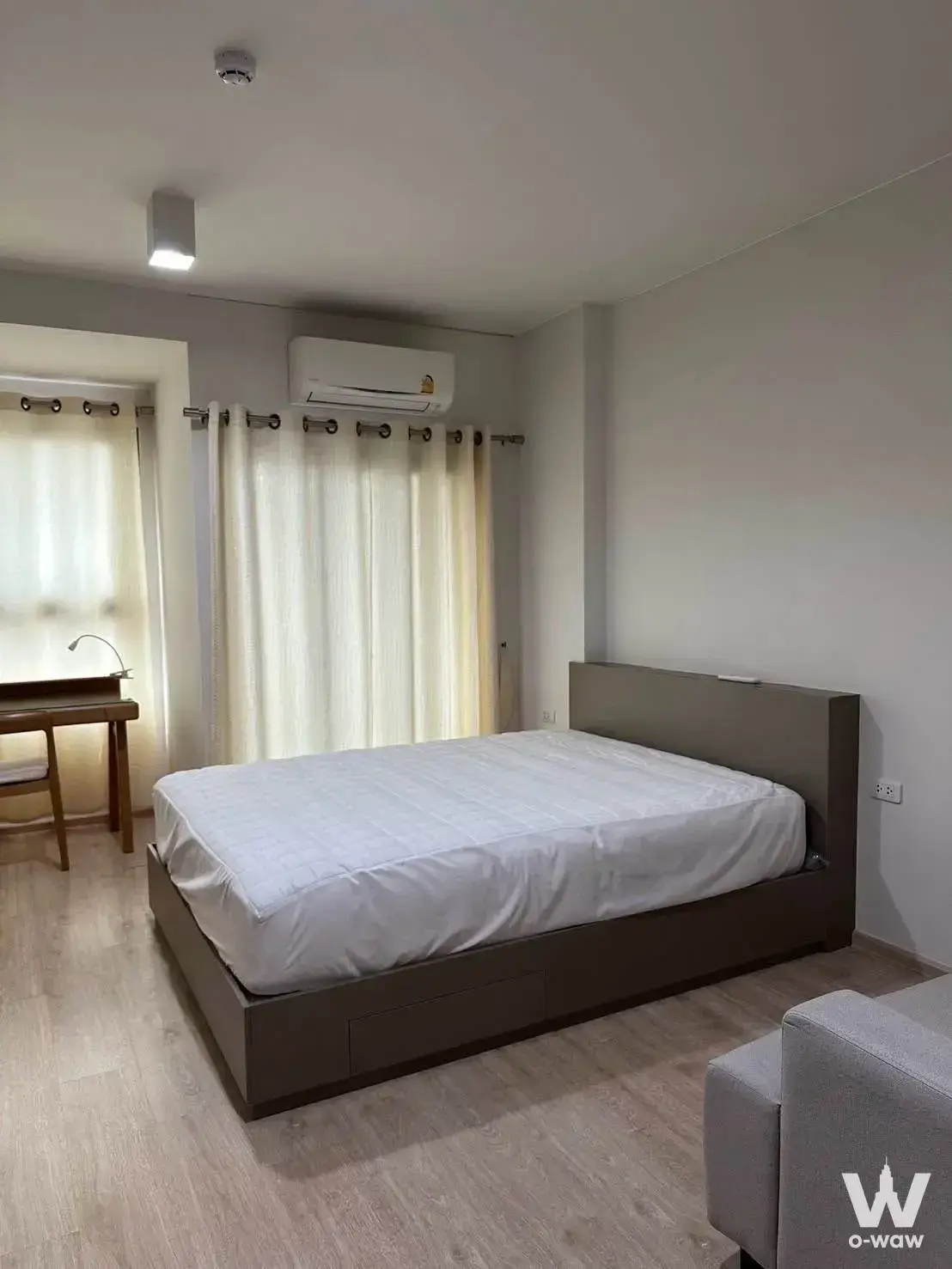 Minimalist bedroom in Ideo Sathon-Wongwian Yai 1-bed unit featuring queen bed, desk, and sheer curtains