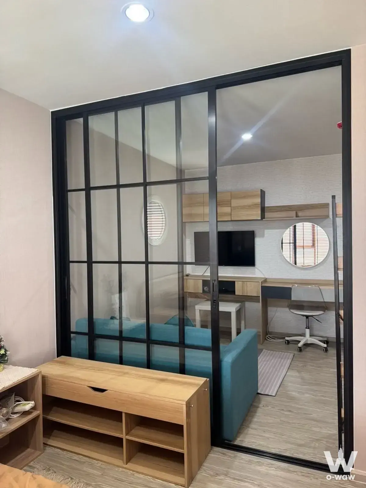 Studio living area with glass partition and teal sofa in RYE Huamak condo