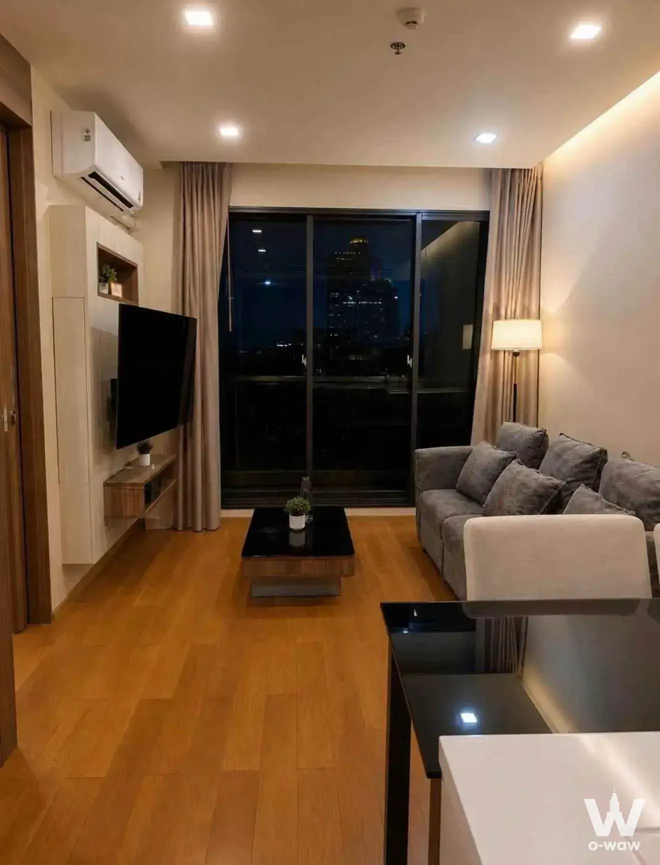 Living room in The Address Sathon condo featuring a grey sofa and night city skyline view