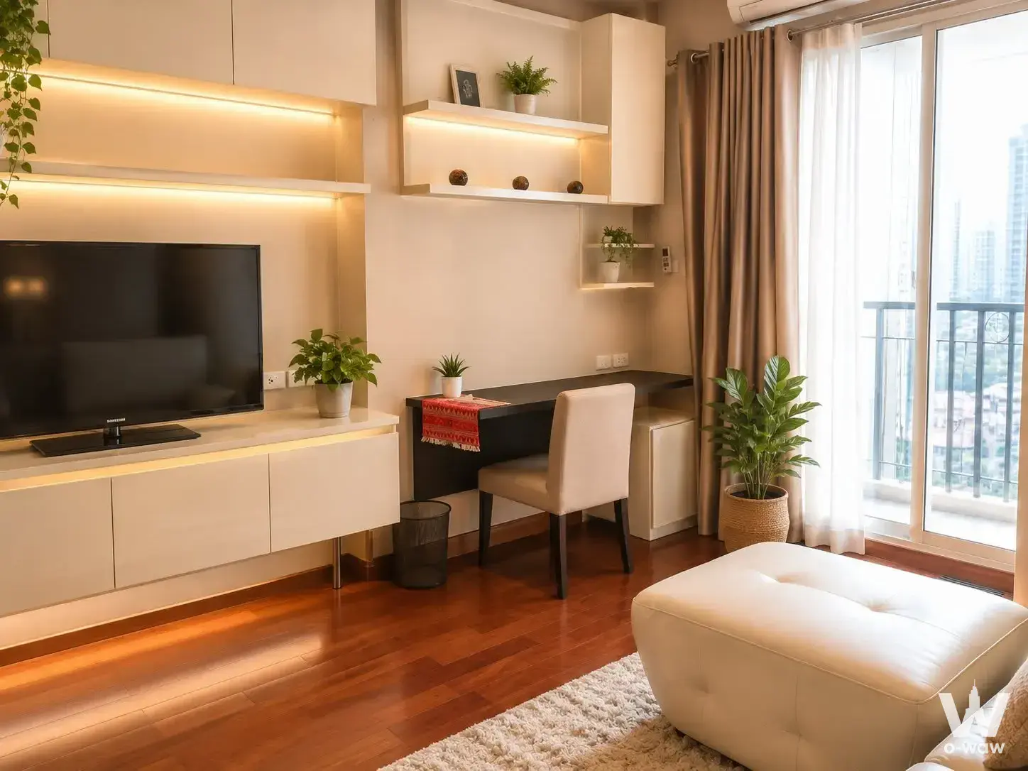 Modern living room in IVY Thonglor condo with glossy wood floors, beige leather ottoman, and balcony city views