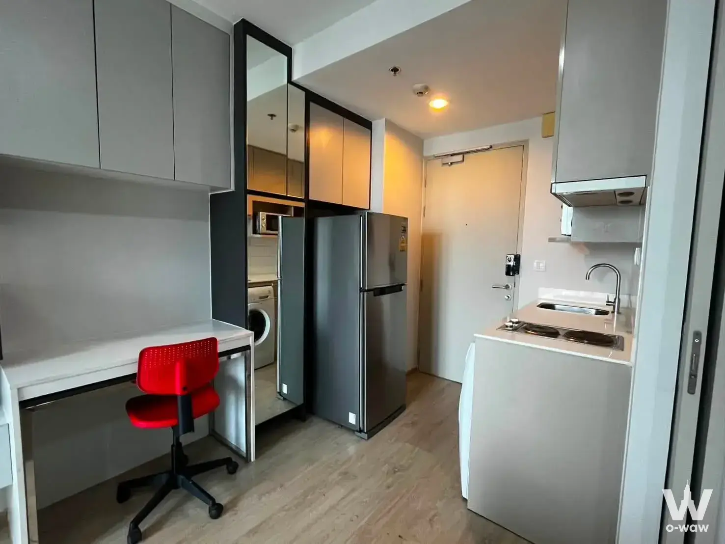 Compact studio interior featuring a built-in desk, red chair, and kitchenette in Ideo Q Ratchathewi