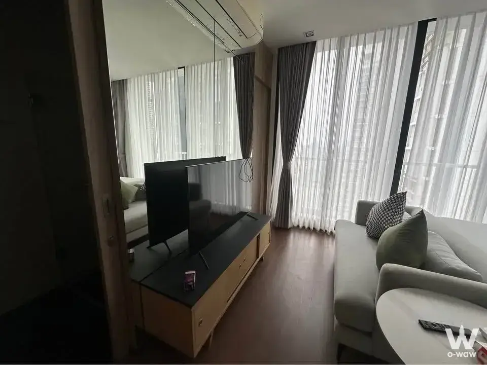Living room with light-grey sofa, city skyline view through floor-to-ceiling windows, and wall-mounted TV