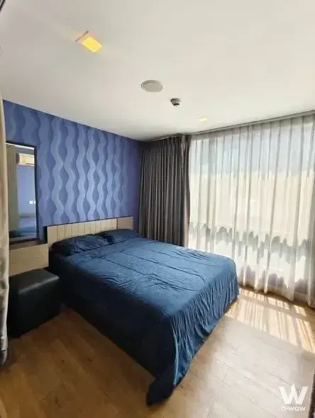 Bedroom in ESTA Bliss Condo 1-bed rental with blue duvet, geometric wallpaper, and light wood headboard paneling