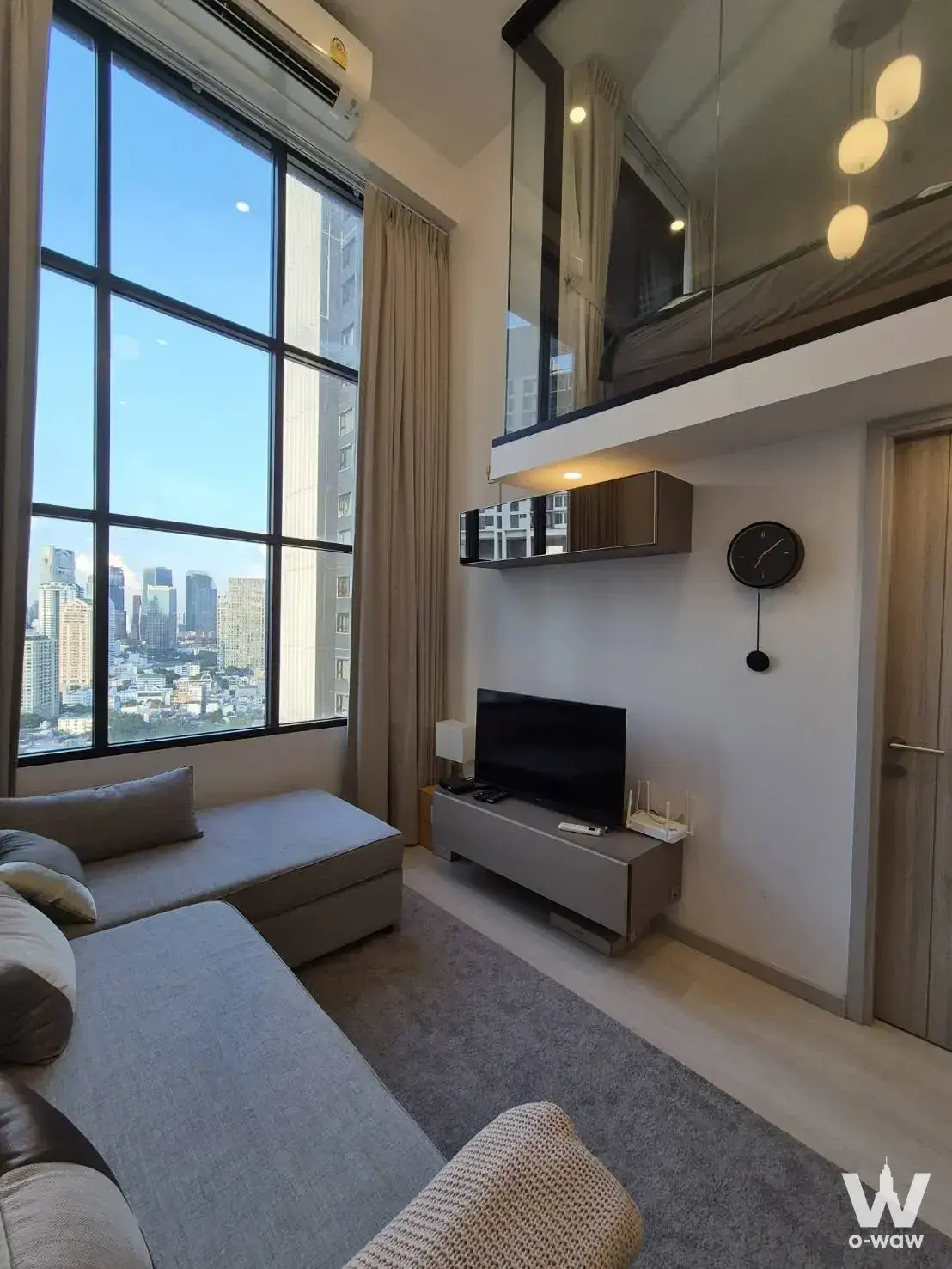 Double-height living room in KnightsBridge Prime Sathon with mezzanine, pendant lights and city skyline view