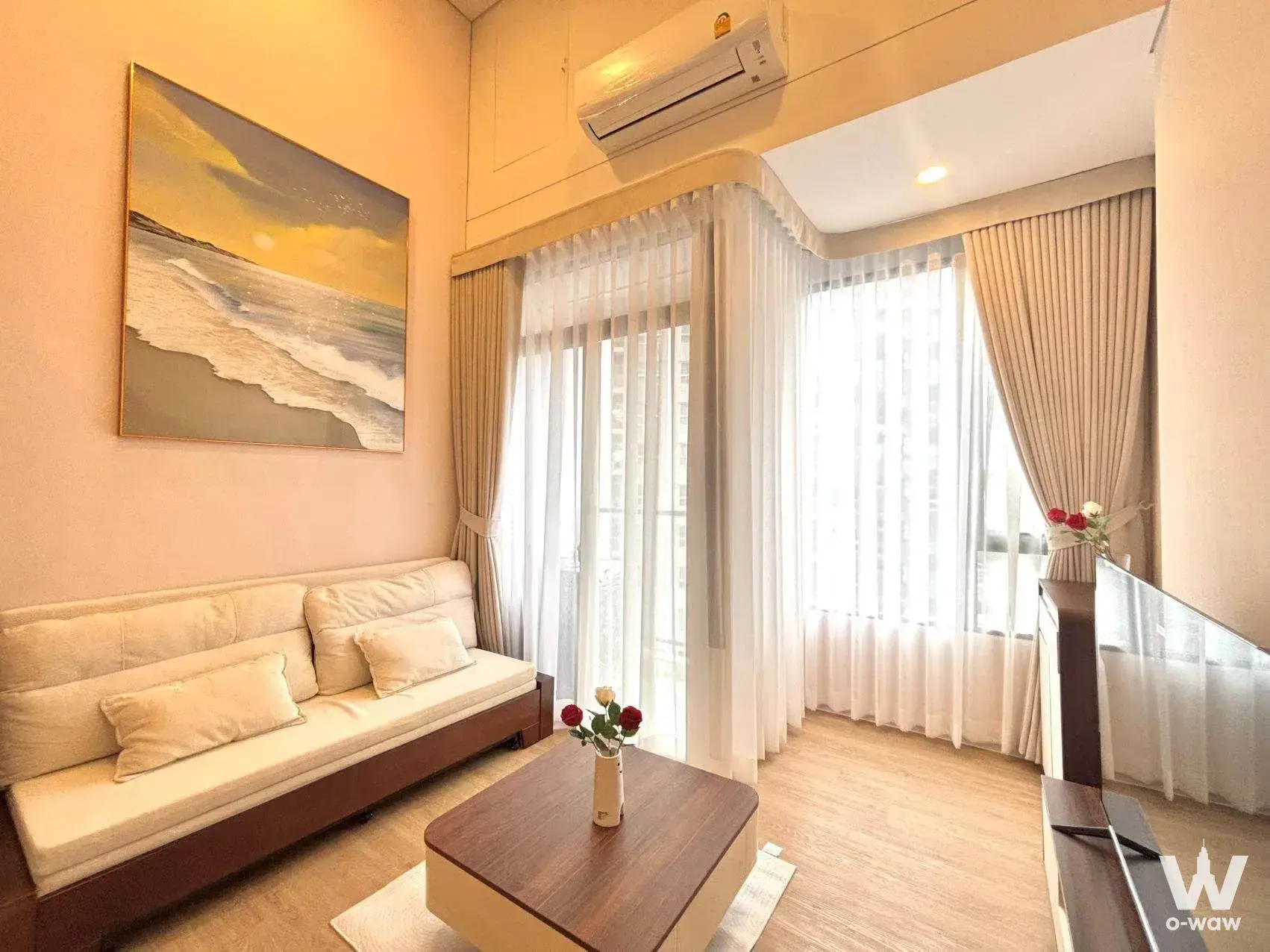 Modern living room with cream sofa, beach sunset canvas art, dark wood coffee table, and sheer curtains letting in light