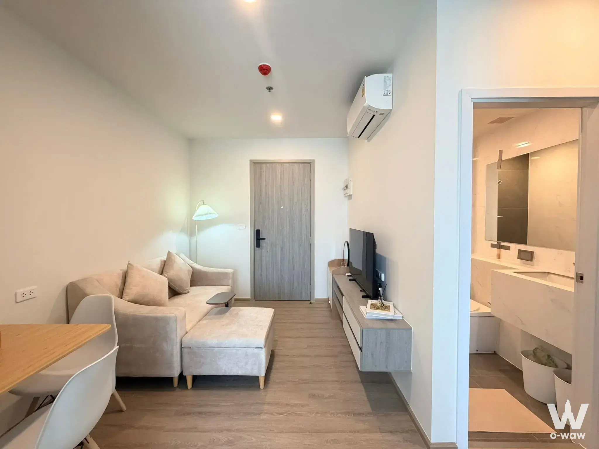 Open-plan living area with beige sectional sofa and wood flooring in Origin Plug & Play Nonthaburi condo