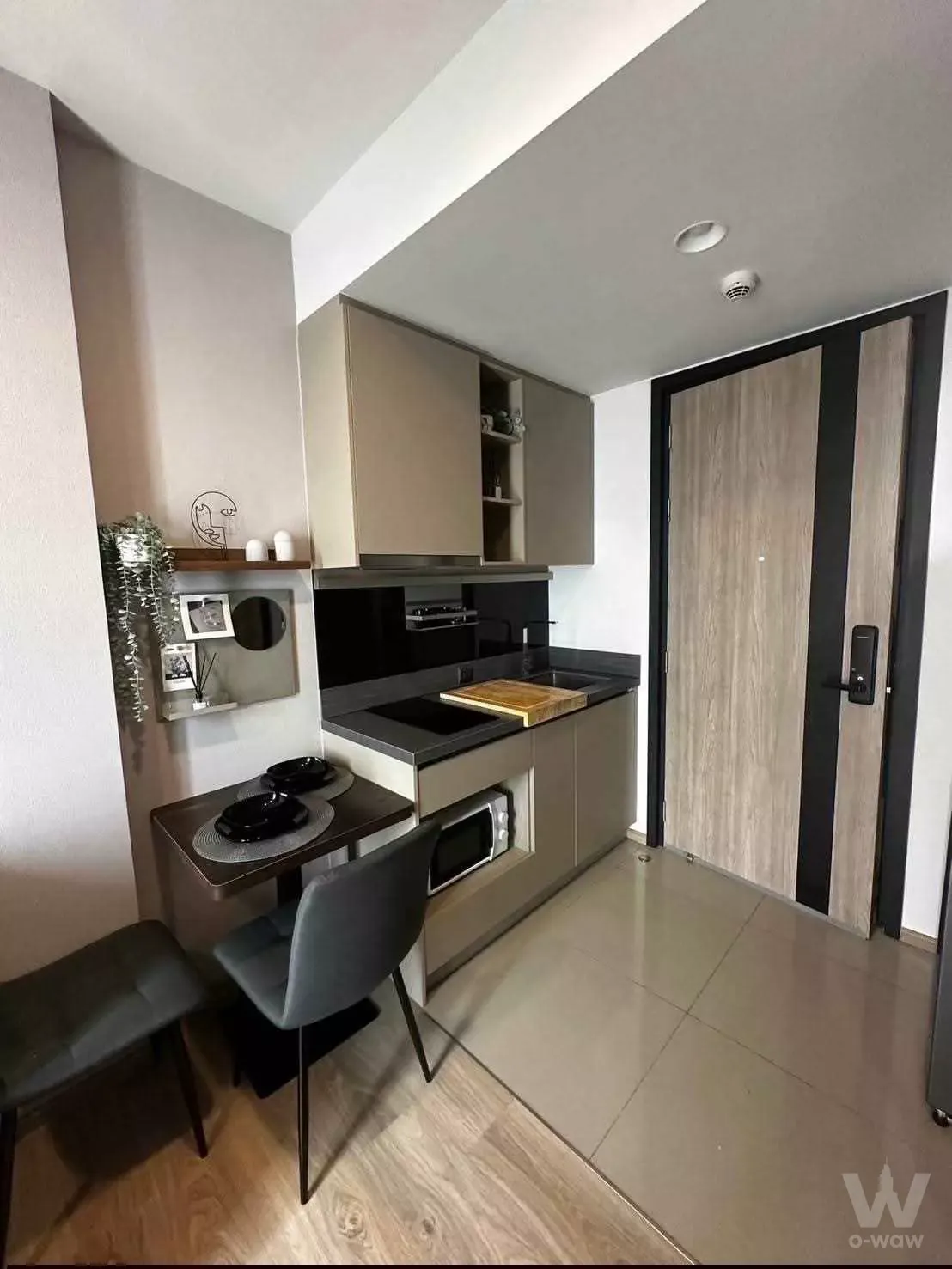 Compact kitchen and dining area with beige cabinets, dark countertop, and smart lock in Oka Haus 1-bed condo