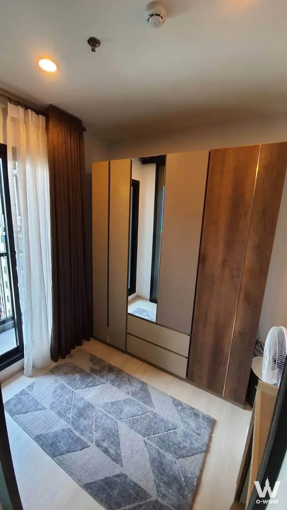 Unfurnished bedroom in Life Asoke condo with walnut wardrobe, mirror, and geometric rug