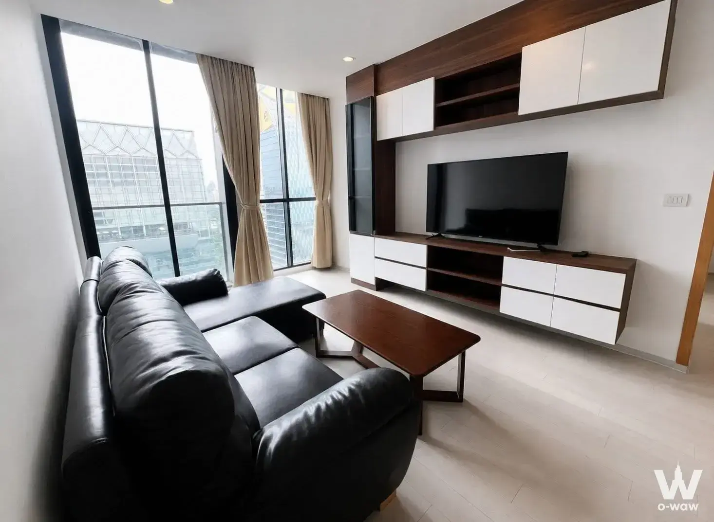 Living room in Noble Ploenchit condo with black leather sectional and city view