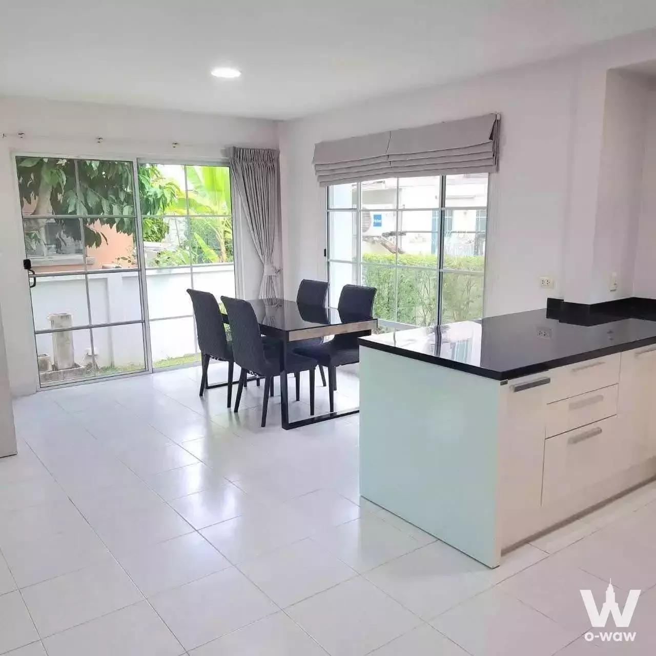 Open-plan dining and kitchen with black glass table and island overlooking greenery in Mantana Onnut house