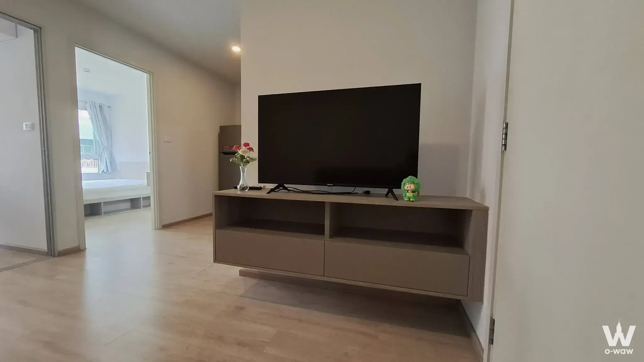 Minimalist living area in Elio Del Moss Phaholyothin condo featuring taupe media console and open bedroom doorway