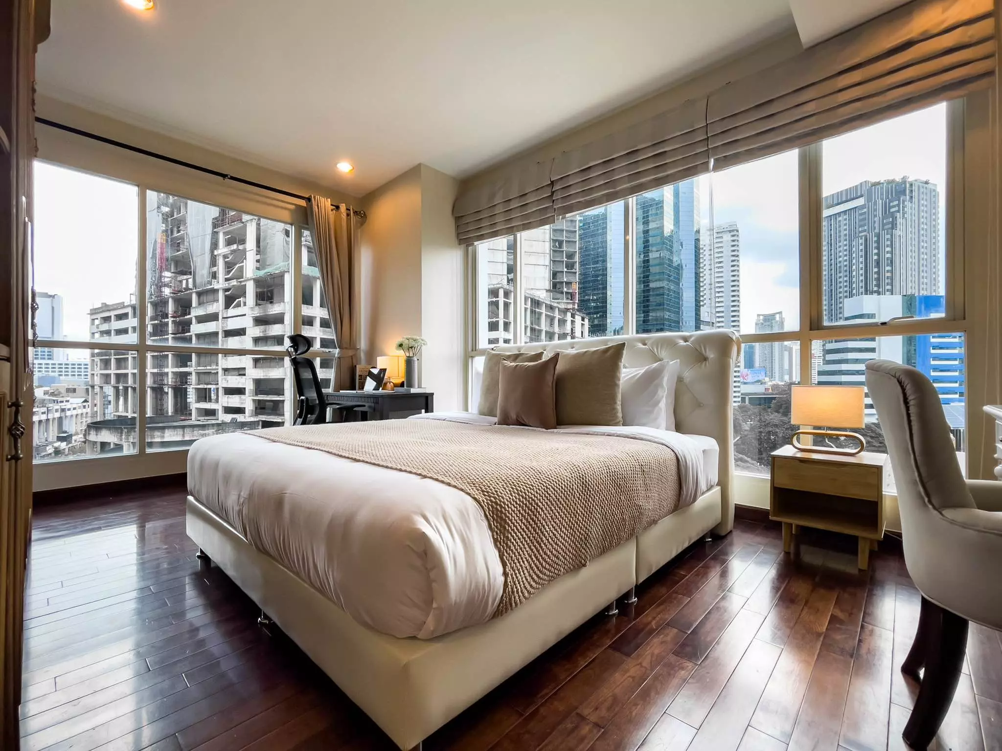 Luxury bedroom in The Address Chidlom 2-bed condo featuring city skyline views, cream bed, and dark hardwood floors