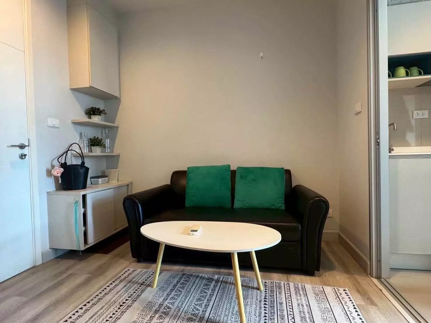 Compact living room with black leather sofa, green pillows, and wood floors in 1-bed condo for rent in Centric Sea Pattaya