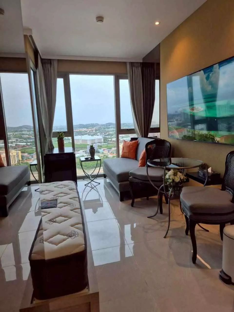 The Riviera Monaco 1-bed condo living room with grey sectional, orange pillows, and floor-to-ceiling windows