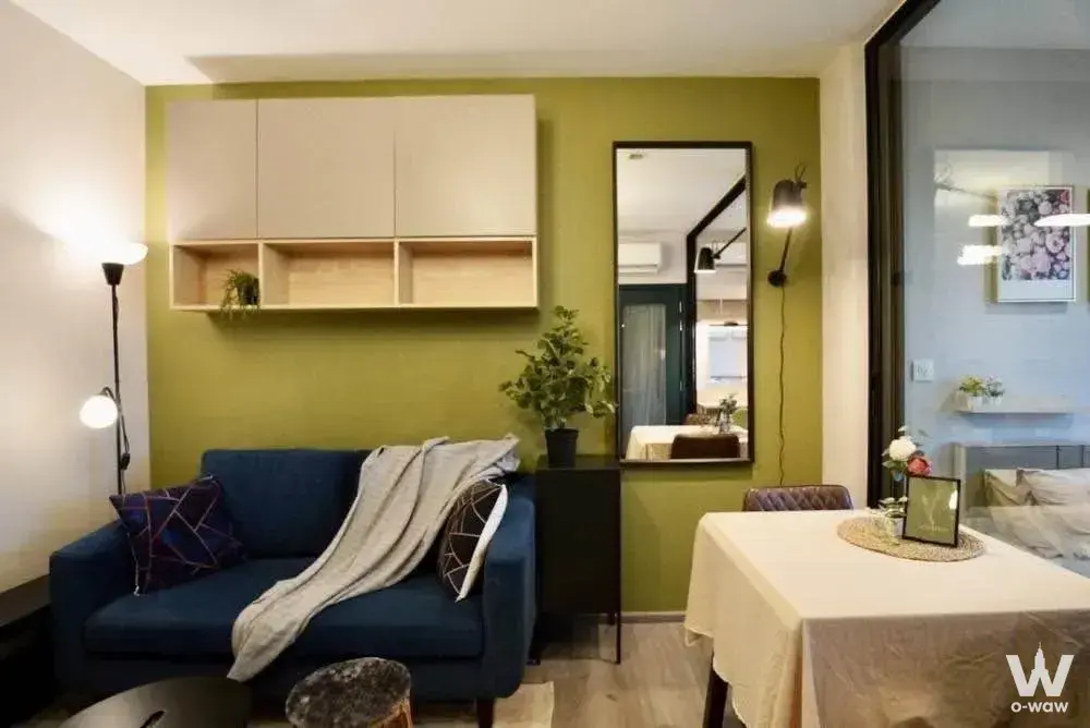 Living room in a 1-bed condo for rent at The Politan Rive with olive accent wall, navy sofa, and dining table