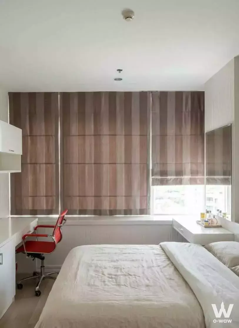 Compact bedroom in TC Green Rama 9 sale listing featuring light wood floors, white walls, and red chair accent