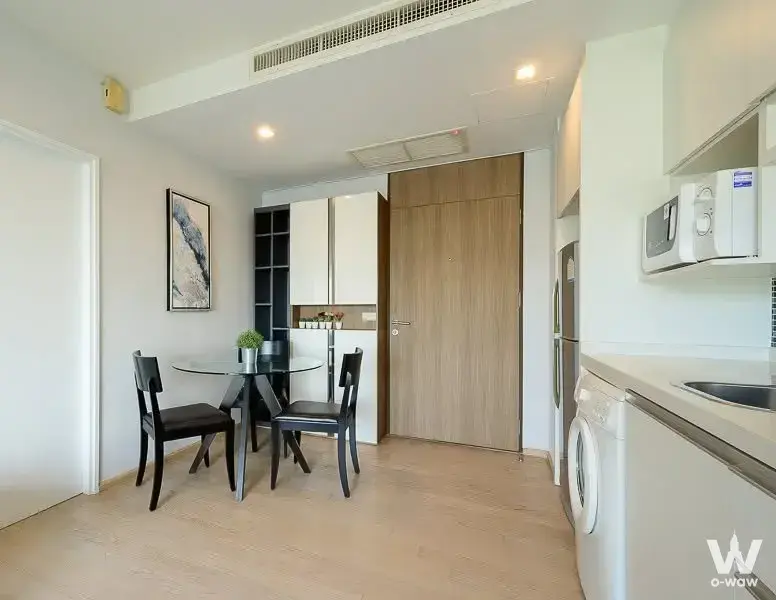 Open-plan studio in Noble Remix rental with glass dining table, built-in shelves, and galley kitchenette