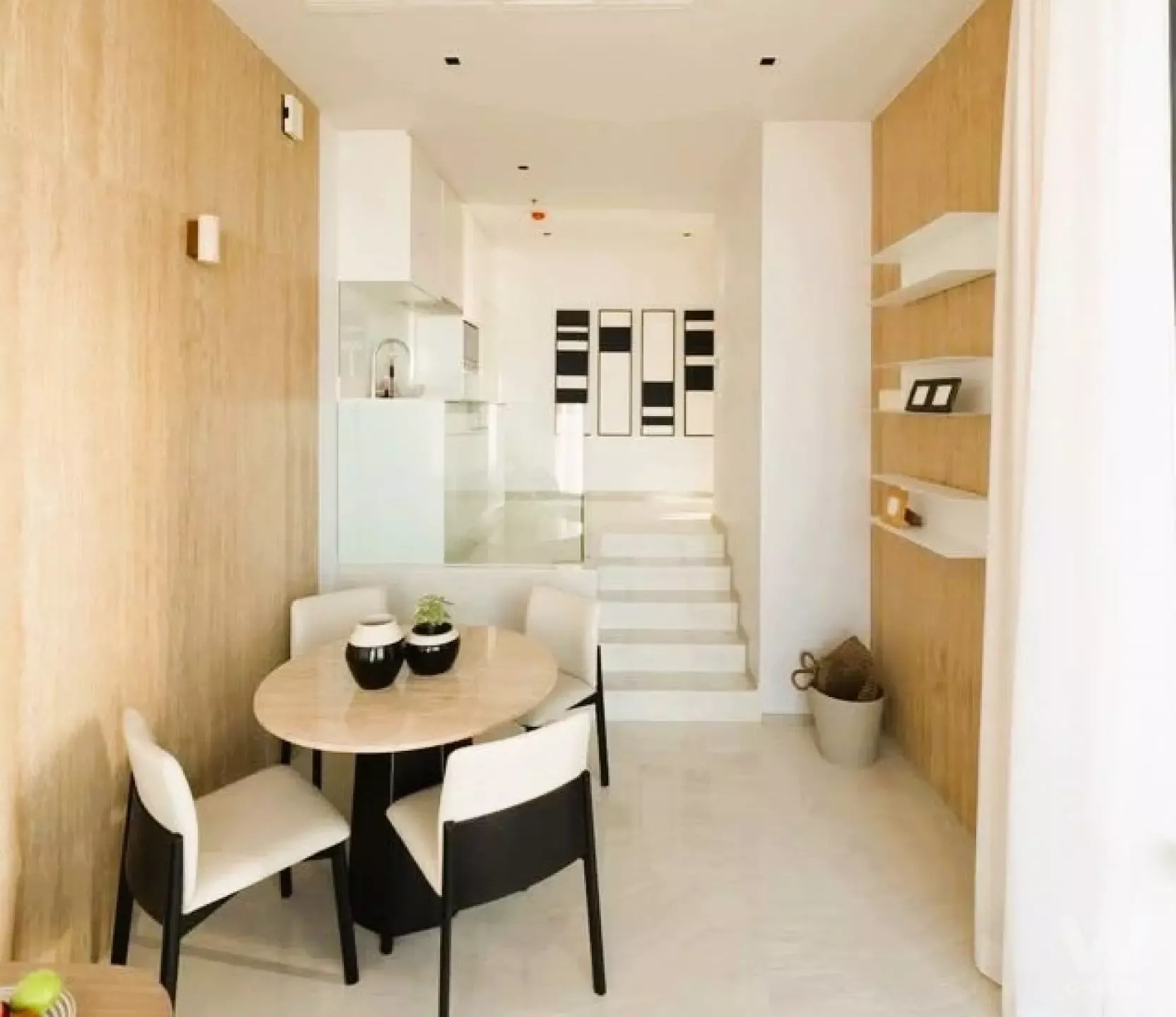Dining area in Ashton Silom 2-bed condo with round wooden table, black-framed chairs, and light wood paneling