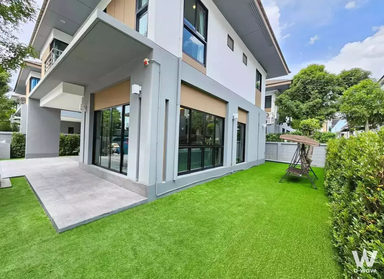 Modern two-story townhouse exterior in Baan Lumpini Suan Luang Rama 9 with white facade, black-framed glass doors, and green