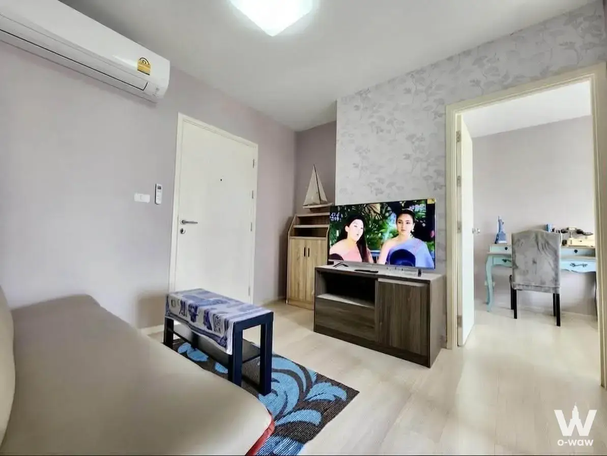 ASPIRE Rattanathibet 2 living room with leather sofa, floral rug, and active flat-screen TV