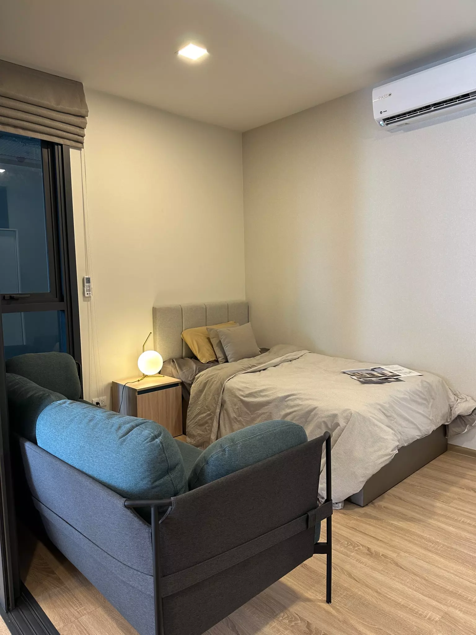 Compact bedroom with grey bed, mustard pillow, and dark sofa in XT Phayathai condo for rent