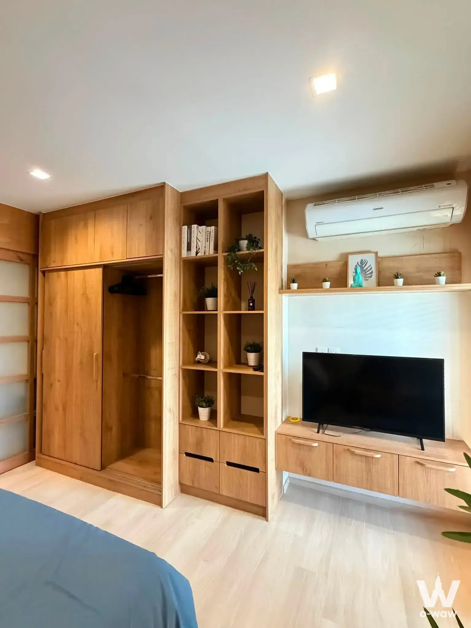 Life One Wireless 1-bed condo bedroom showcasing light-oak built-in cabinetry, open shelving, and TV console