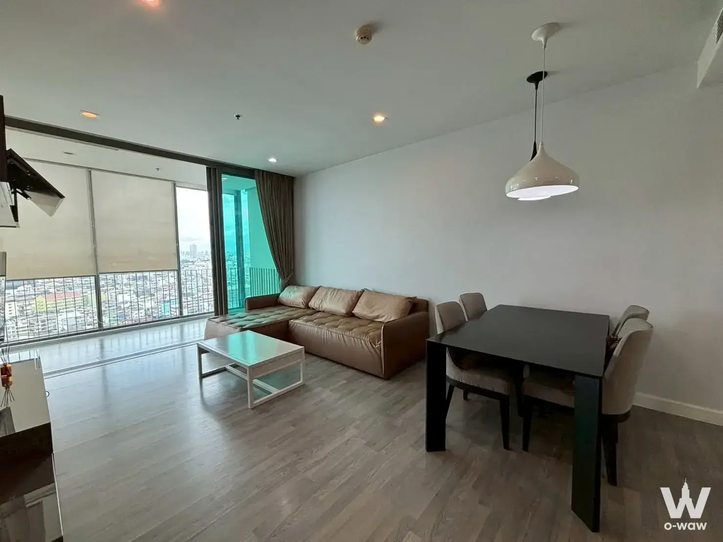 Modern 2-bed condo living room in The Room Rama 4 with leather sofa, city view, and light-grey wood floors