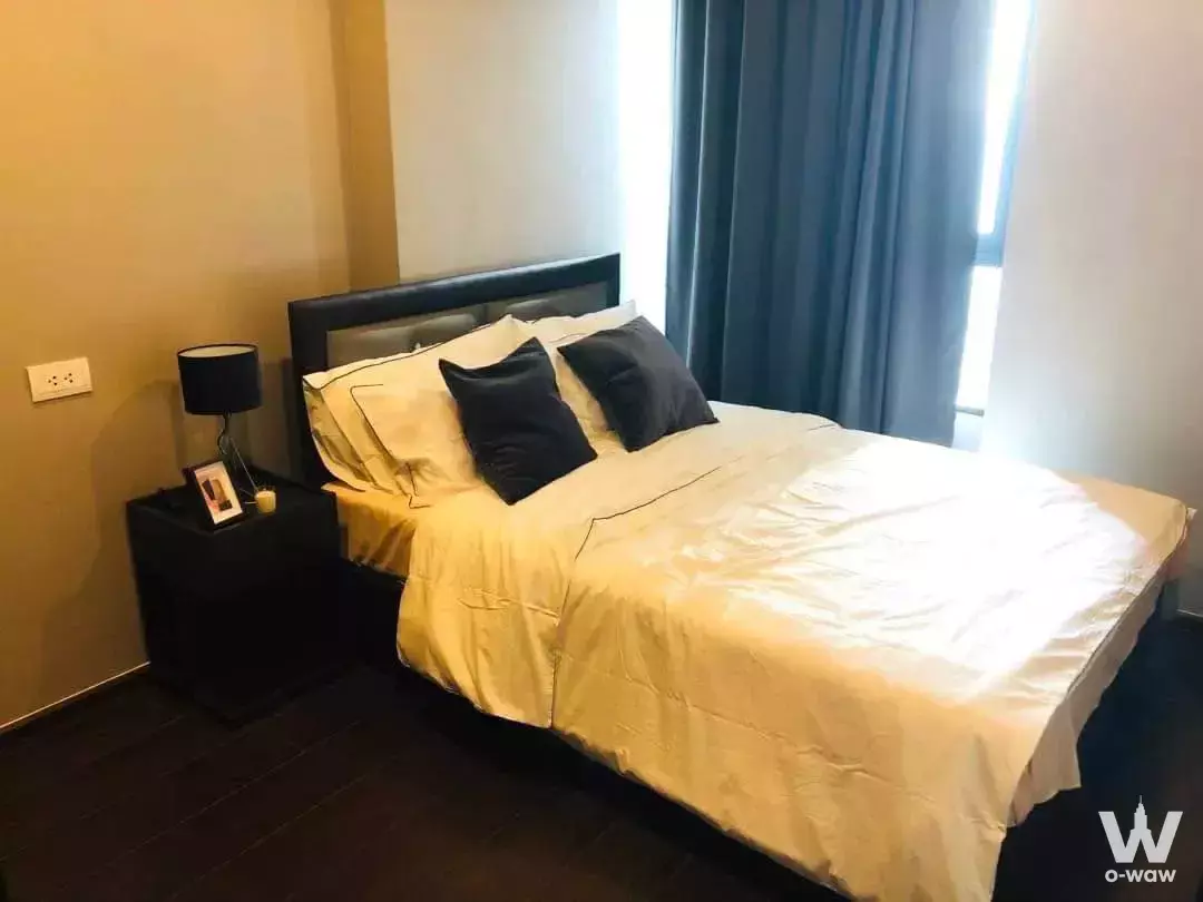 Modern bedroom with black leather headboard, dark wood floors, and slate-blue curtains in C Ekkamai condo
