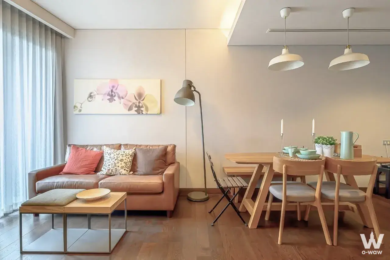 Open-plan living area in The Lumpini 24 with tan leather sofa and light wood dining set