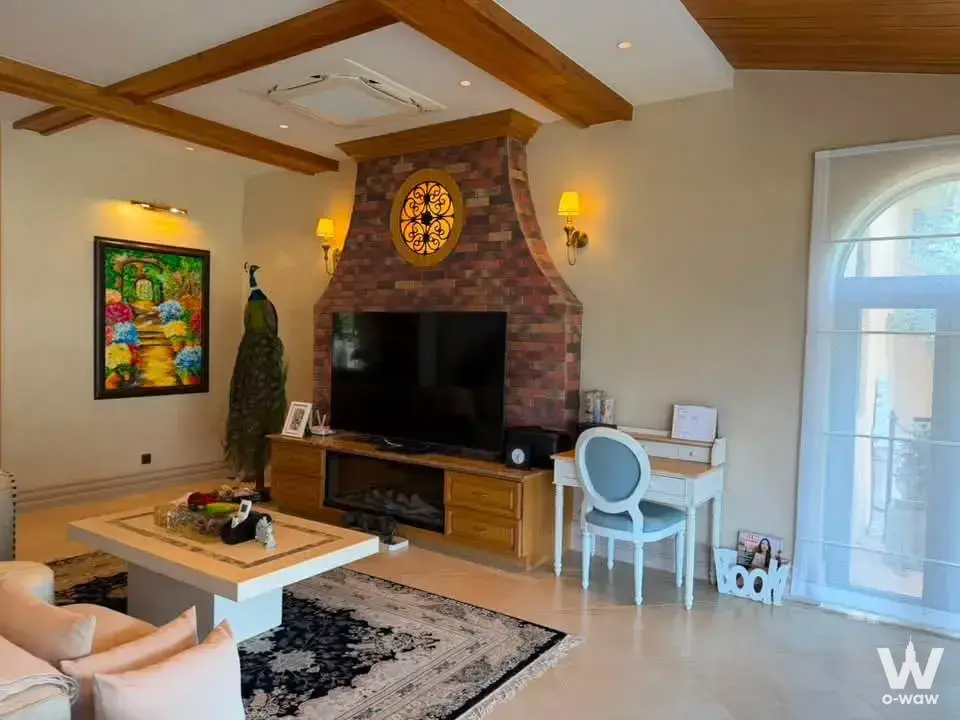 Spacious living room with brick fireplace, TV console, peacock statue, and arched glass door
