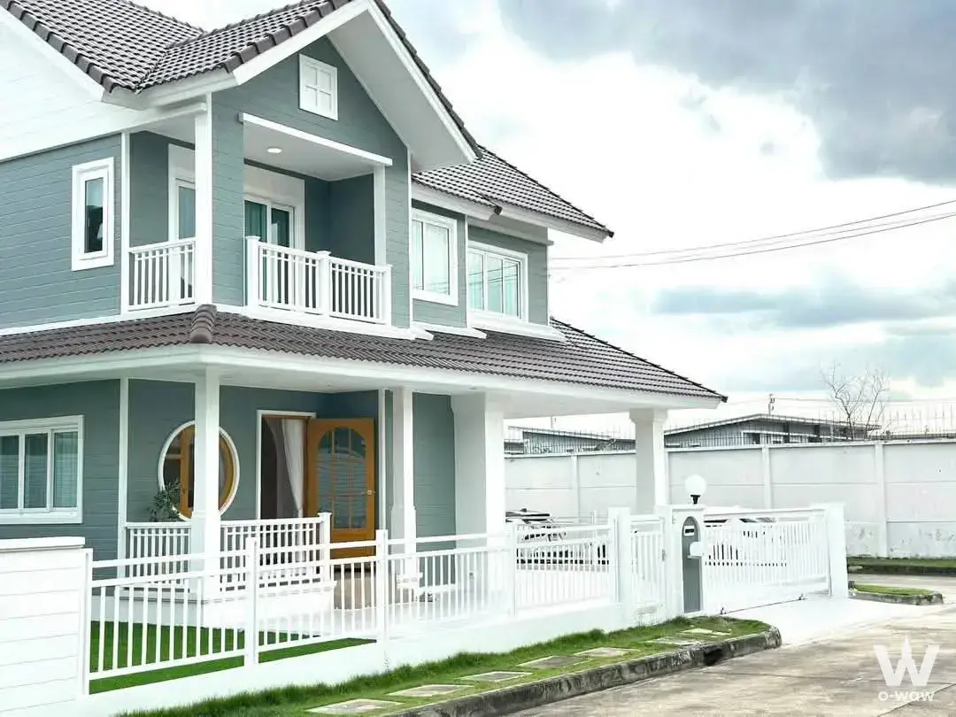Two-story detached house exterior at Burasiri Panya-Indra with grey siding, brown tile roof, and white porch columns