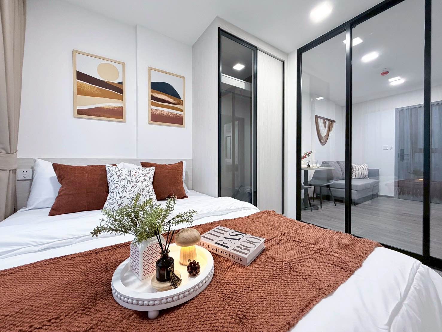 Cozy bedroom with white linens, rust-orange accents, and glass sliding doors in Kave Wonderland condo for rent