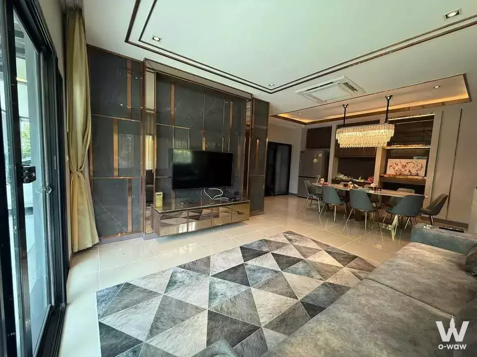 Baan Lumpini living area with grey sofa, geometric marble rug, gold-accented stone wall, and crystal chandelier