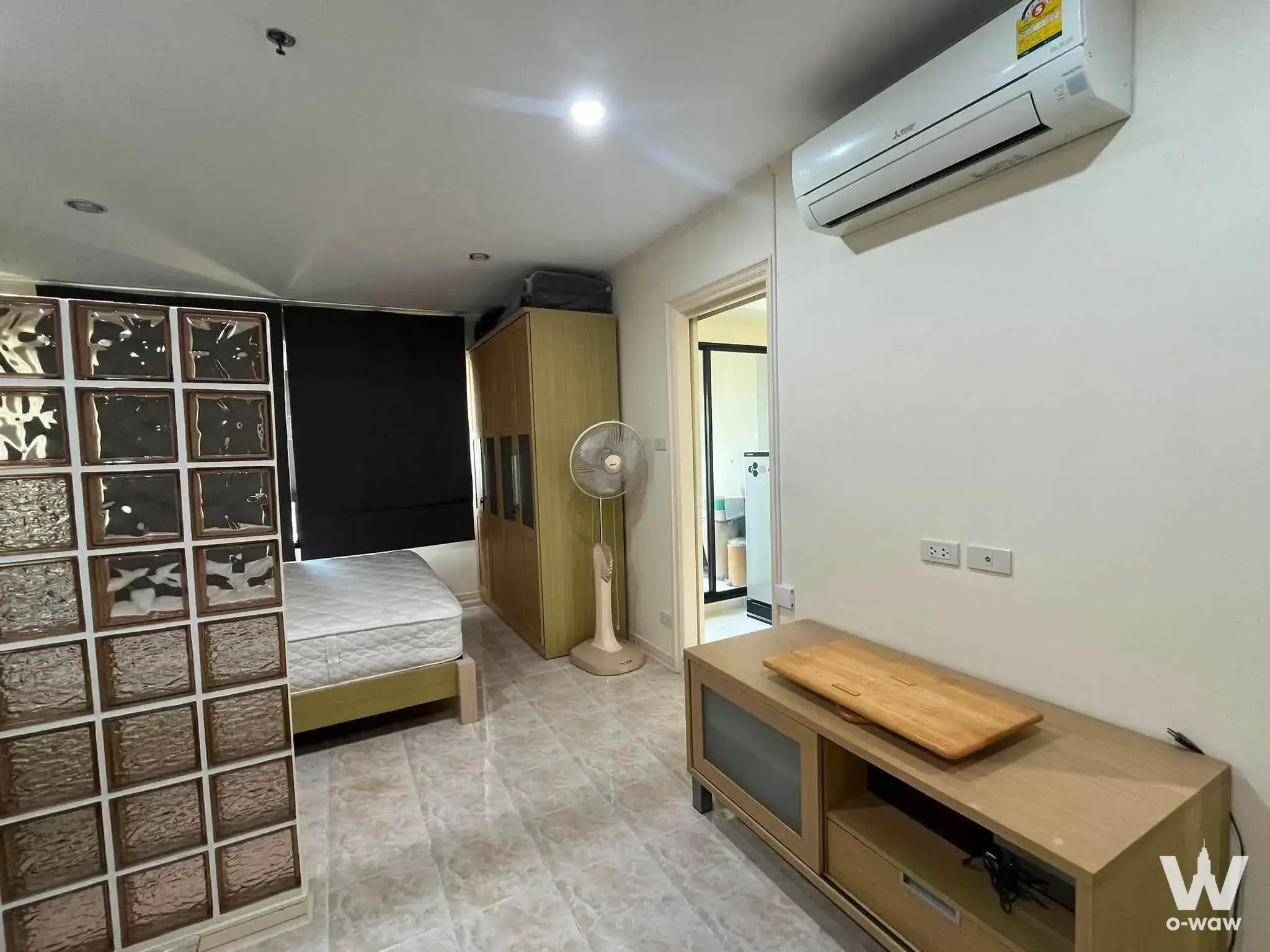 Minimalist bedroom in a Lumpini Place Rama 3 condo featuring a glass block partition and light wood wardrobe