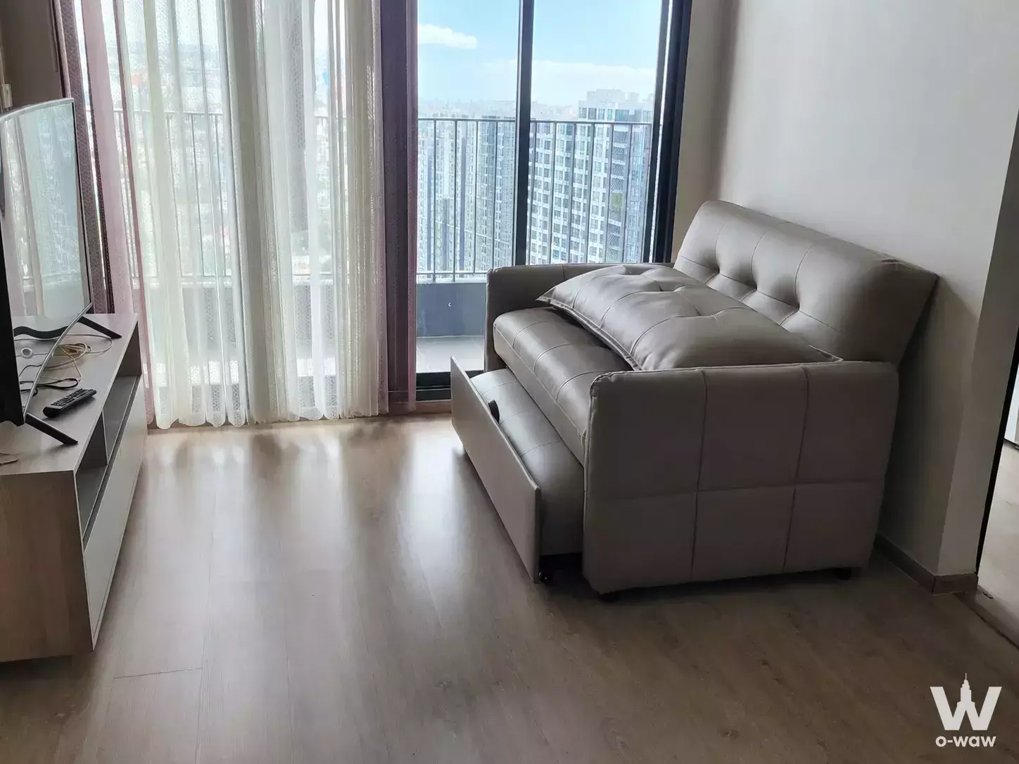 Living room in Ideo O2 condo with sofa bed, media console, and city view