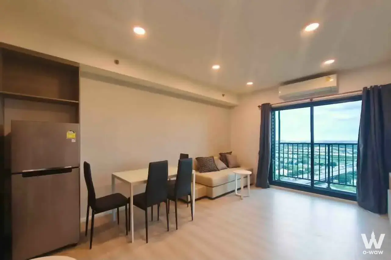 Open-plan living area in A Space Mega 1 condo featuring beige sofa and city view balcony