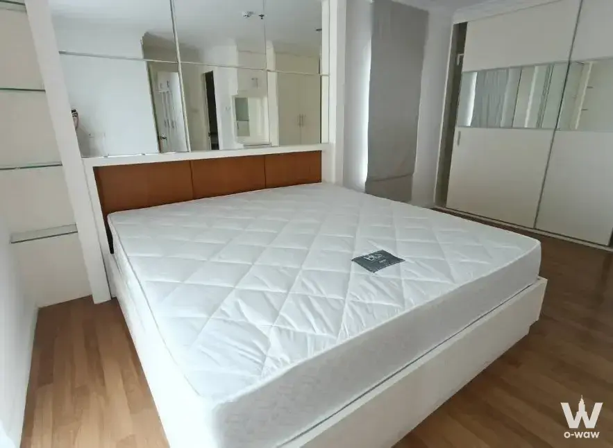Bedroom in a Lumpini Place Rama 9 condo featuring wood headboard and mirrored panels behind the bed