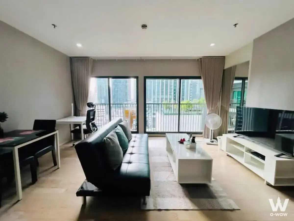 Open-plan living room with black leather sofa, teal pillows, and balcony access in Noble Remix condo