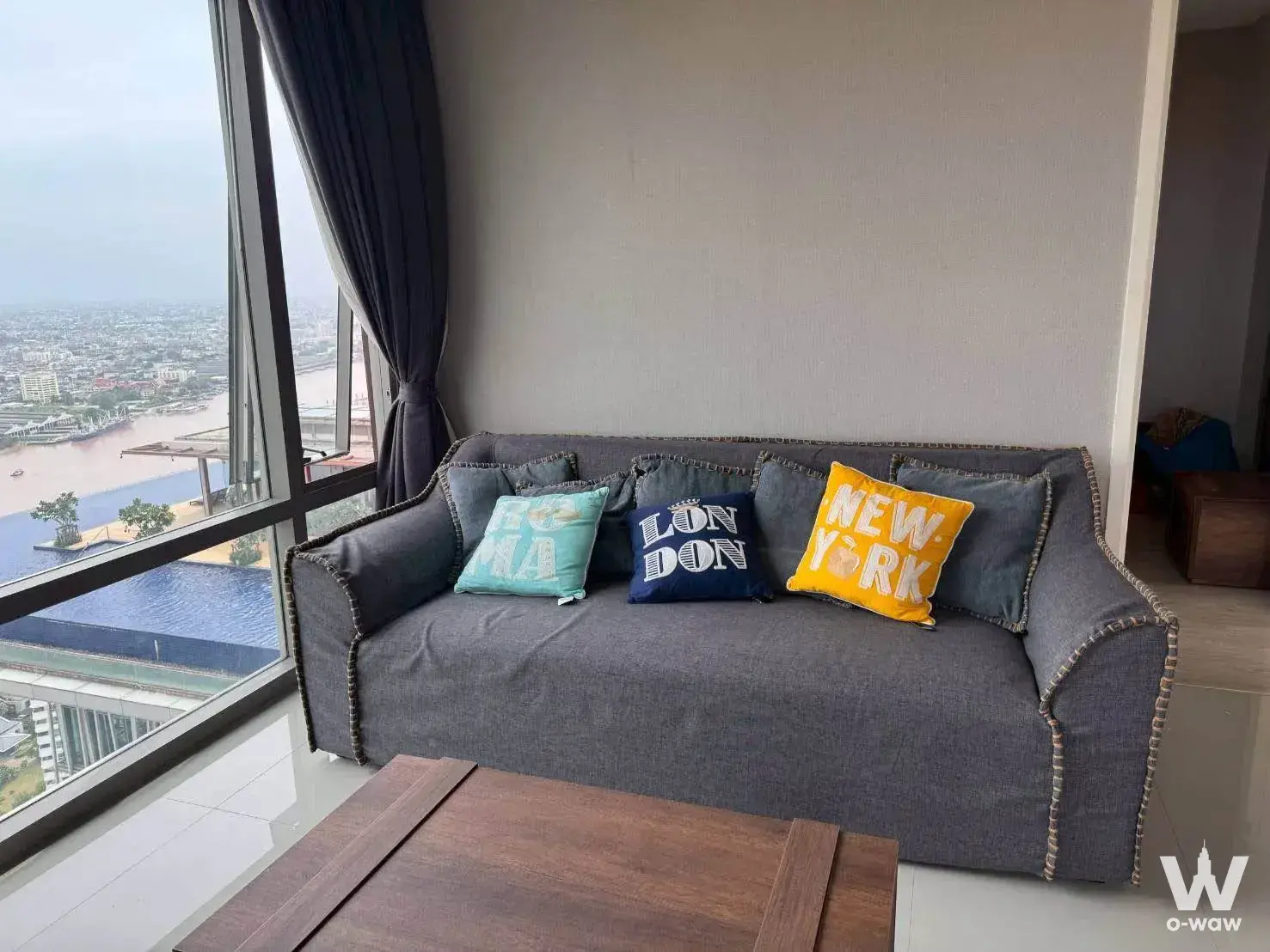Living room with grey sofa and river view from infinity pool terrace at StarView Rama 3