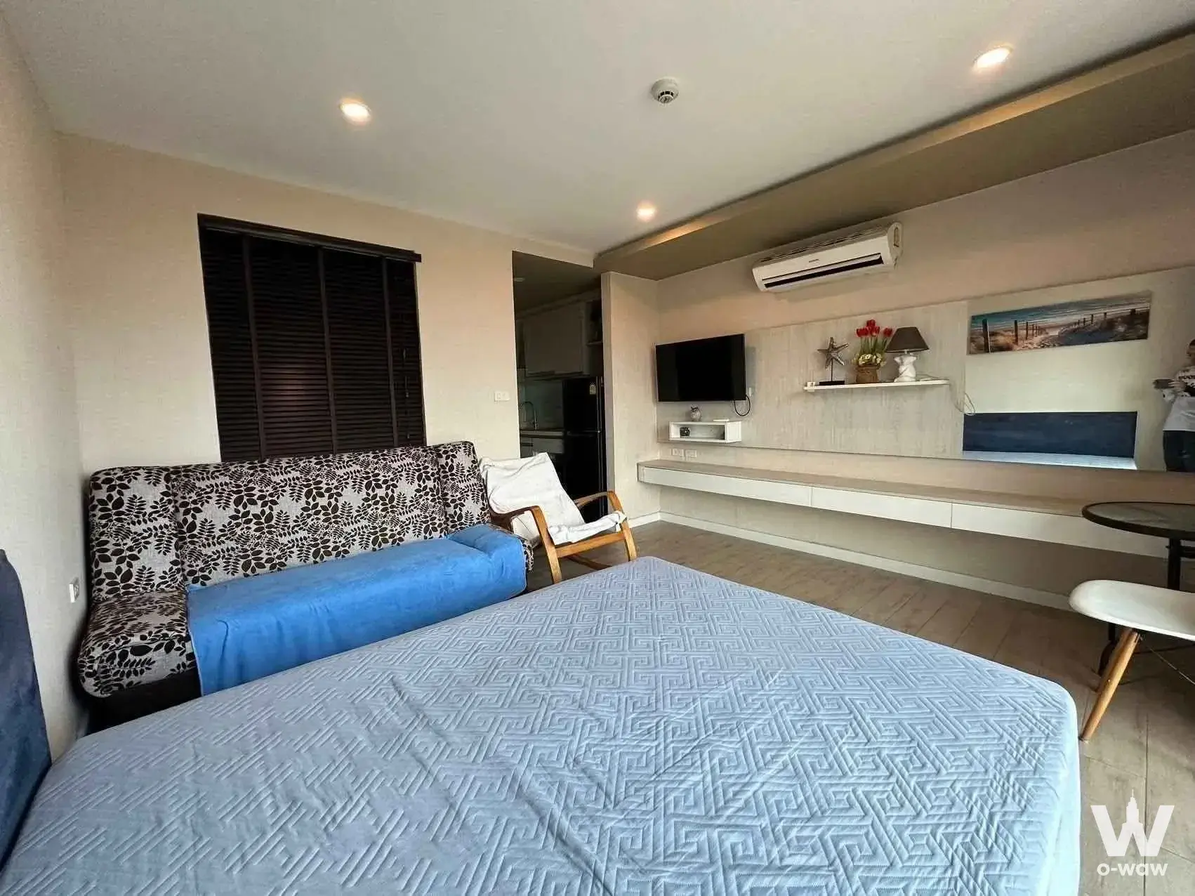 Studio bedroom with blue bedspread and floral sofa near window in Seven Seas Condo Jomtien